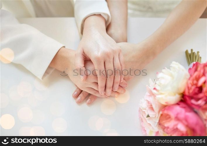 people, homosexuality, same-sex marriage and love concept - close up of happy married lesbian couple hands over holiday lights background