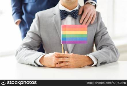 people, homosexuality, same-sex marriage and love concept - close up of happy male gay couple in suits and bow-ties with wedding ring holding rainbow flag