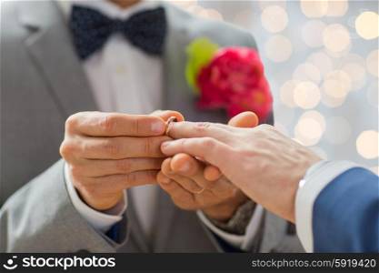 people, homosexuality, same-sex marriage and love concept - close up of happy male gay couple hands putting wedding ring on lights background