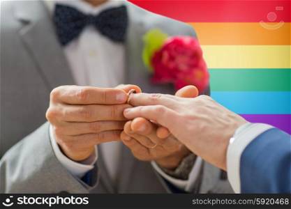 people, homosexuality, same-sex marriage and love concept - close up of happy male gay couple hands putting wedding ring on over rainbow flag background