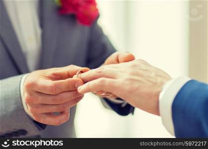 people, homosexuality, same-sex marriage and love concept - close up of happy male gay couple hands putting wedding ring on