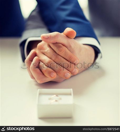 people, homosexuality, same-sex marriage and love concept - close up of happy male gay couple holding hands and wedding rings in box on table