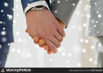 people, homosexuality, same-sex marriage and love concept - close up of happy male gay couple holding hands with wedding rings on over snow effect