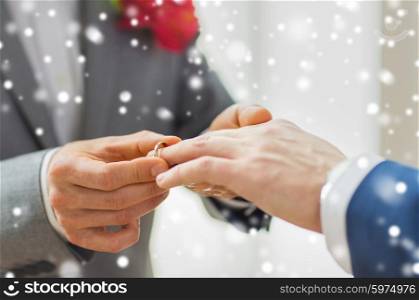 people, homosexuality, same-sex marriage and love concept - close up of happy male gay couple hands putting wedding ring on over snow effect