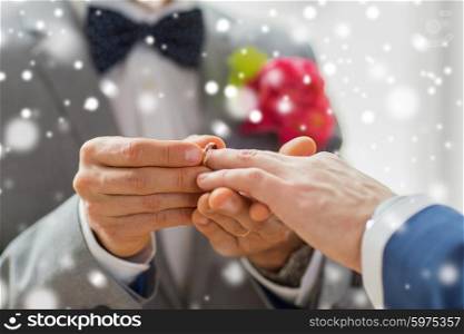 people, homosexuality, same-sex marriage and love concept - close up of happy male gay couple hands putting wedding ring on over snow effect