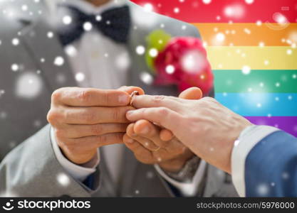 people, homosexuality, same-sex marriage and love concept - close up of happy male gay couple hands putting wedding ring on over rainbow flag background and snow effect