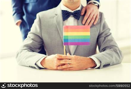 people, homosexuality, same-sex marriage and love concept - close up of happy male gay couple in suits and bow-ties with wedding ring holding rainbow flag