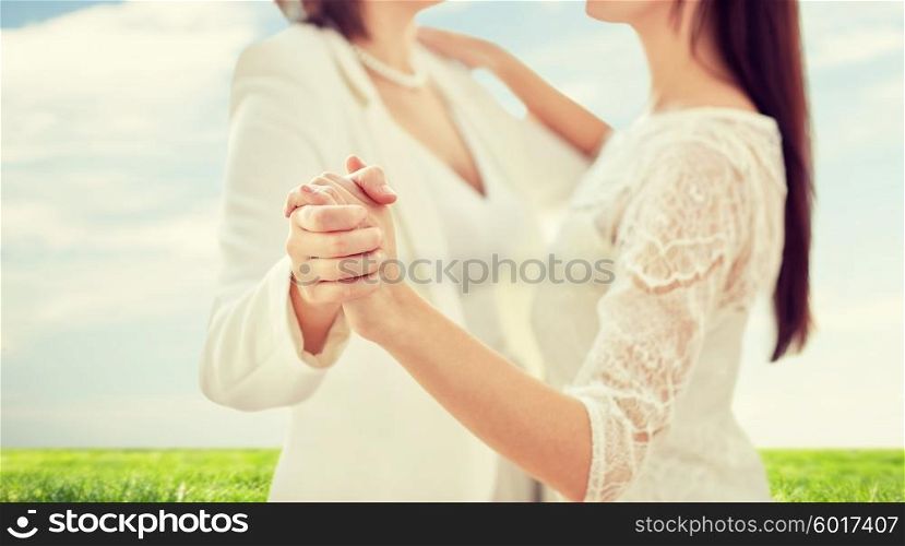 people, homosexuality, same-sex marriage and love concept - close up of happy married lesbian couple dancing over blue sky and grass background