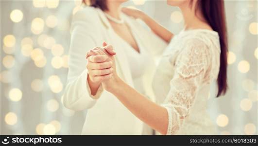 people, homosexuality, same-sex marriage and love concept - close up of happy married lesbian couple dancing over holiday lights background
