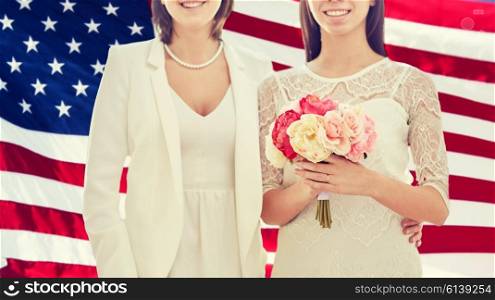 people, homosexuality, same-sex marriage and love concept - close up of happy married lesbian couple with flower bunch over american flag background