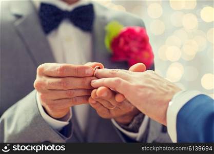 people, homosexuality, same-sex marriage and love concept - close up of happy male gay couple hands putting wedding ring on lights background