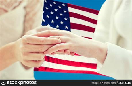 people, homosexuality, same-sex marriage and love concept - close up of happy lesbian couple hands putting on wedding ring over american flag background