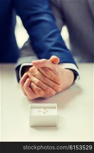 people, homosexuality, same-sex marriage and love concept - close up of happy male gay couple holding hands and wedding rings in box on table