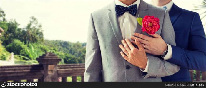 people, homosexuality, same-sex marriage and love concept - close up of happy married male gay couple in suits with buttonholes and bow-ties on wedding over balcony and nature background