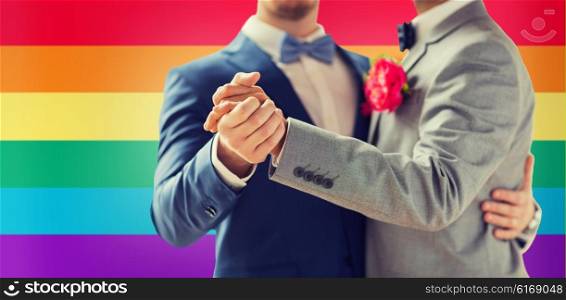 people, homosexuality, same-sex marriage and love concept - close up of happy male gay couple holding hands and dancing on wedding over rainbow flag background