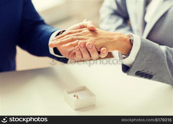 people, homosexuality, same-sex marriage and love concept - close up of happy male gay couple hands with wedding ring on and little box on table