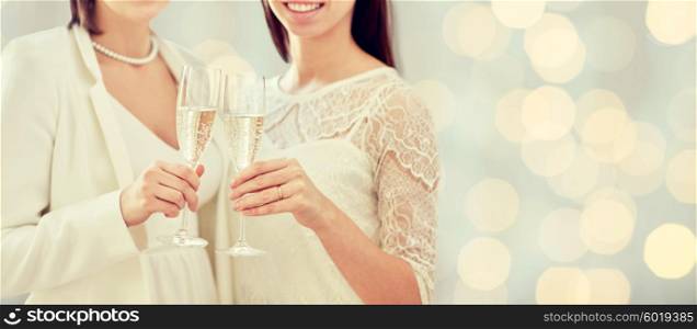 people, homosexuality, same-sex marriage, celebration and love concept - close up of happy married lesbian couple holding and clinking champagne glasses over holidays lights background