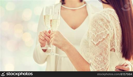 people, homosexuality, same-sex marriage, celebration and love concept - close up of happy married lesbian couple holding and clinking champagne glasses over holiday lights background