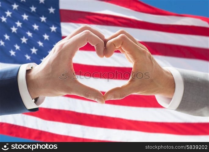people, homosexuality, same-sex marriage, gesture and love concept - close up of happy male gay couple hands showing heart hand sign over american flag background