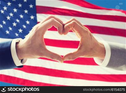people, homosexuality, same-sex marriage, gesture and love concept - close up of happy male gay couple hands showing heart hand sign over american flag background