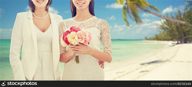 people, homosexuality, same-sex marriage, honeymoon and love concept - close up of happy married lesbian couple with flower bunch over tropical beach background