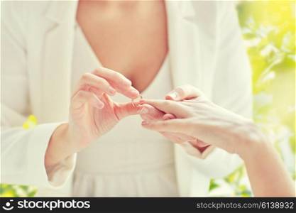 people, homosexuality, same-sex marriage, summer and love concept - close up of happy lesbian couple hands putting on wedding ring over green tree leavers background