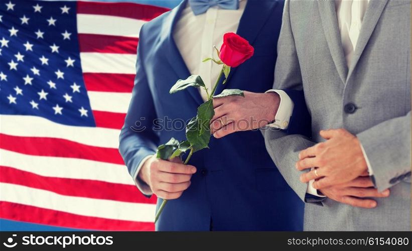 people, homosexuality, same-sex marriage, travel and gay love concept - close up of happy male gay couple with red rose flower holding hands on wedding over american flag background