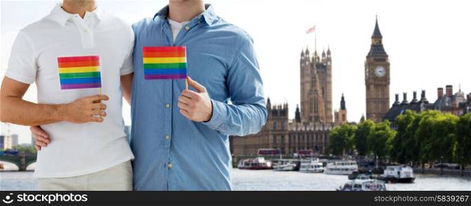 people, homosexuality, same-sex marriage, travel and love concept - close up of male gay couple holding rainbow flags and hugging from back over big ben and houses of parliament in london background
