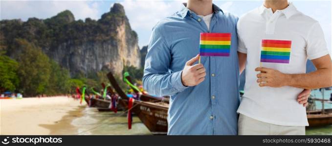 people, homosexuality, same-sex marriage, travel and love concept - close up of happy male gay couple holding rainbow flags and hugging over thailand beach background