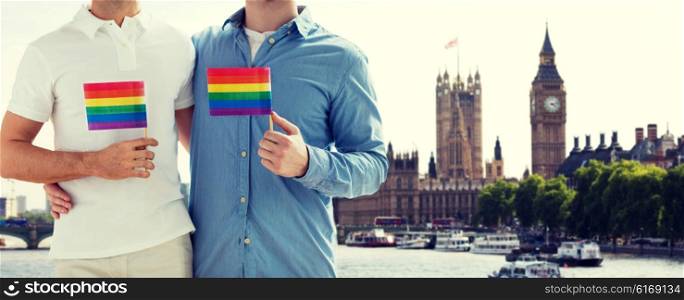 people, homosexuality, same-sex marriage, travel and love concept - close up of male gay couple holding rainbow flags and hugging from back over big ben and houses of parliament in london background
