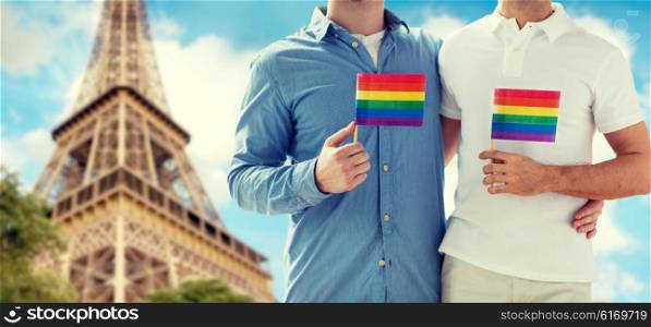 people, homosexuality, same-sex marriage, travel and love concept - close up of happy male gay couple holding rainbow flags and hugging from back over paris eiffel tower background
