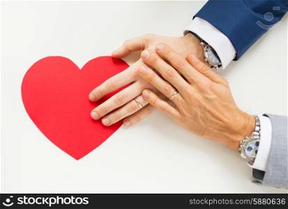 people, homosexuality, same-sex marriage, valentines day and love concept - close up of happy married male gay couple hands with red paper heart shape on table