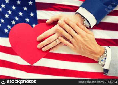 people, homosexuality, same-sex marriage, valentines day and love concept - close up of happy married male gay couple hands with red paper heart shape over american flag background