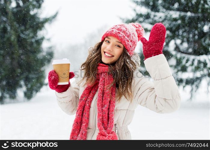 people, hot drinks and christmas concept - happy teenage girl or young woman drinking takeaway coffee outdoors in winter park. happy teenage girl with coffee in winter park