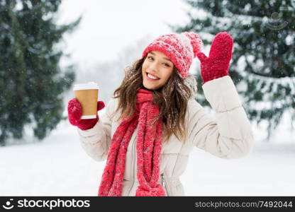 people, hot drinks and christmas concept - happy teenage girl or young woman drinking takeaway coffee outdoors in winter park. happy teenage girl with coffee in winter park