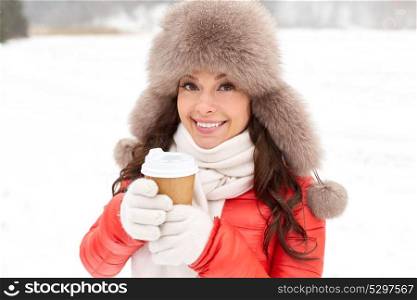 people, hot drinks and leisure concept - happy woman in winter fur with coffee cup hat outdoors. happy woman in winter fur hat with coffee outdoors