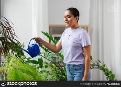 people, housekeeping and plants care concept - african american woman watering houseplants at home. african american woman watering plants at home