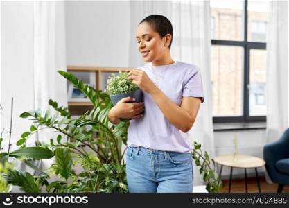 people, housekeeping and plants care concept - african american woman with houseplants at home. african american woman with plants at home
