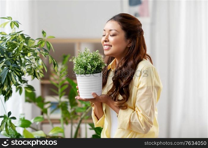 people, housekeeping and plants care concept - happy asian woman with flower in pot at home. happy asian woman with flower in pot at home