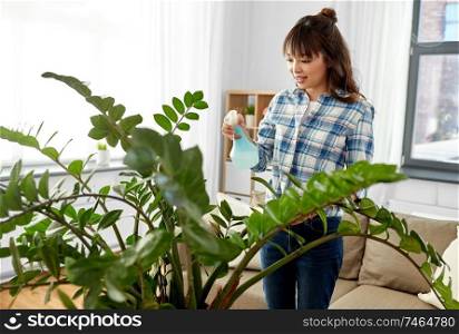 people, housework and care concept - happy asian woman or housewife spraying houseplants with water sprayer at home. happy asian woman spraying houseplants at home