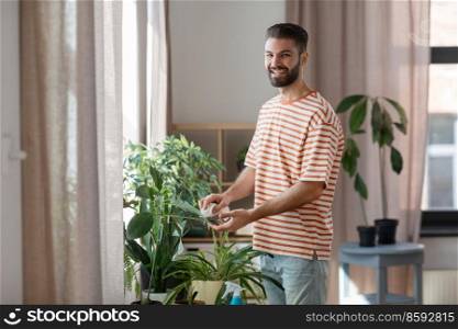 people, housework and care concept - happy man with tissue cleaning houseplant’s leaves at home. man cleaning houseplant with tissue at home