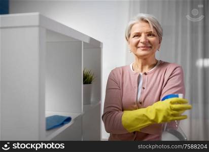people, housework and cleaning concept - happy senior woman in rubber gloves with detergent at home rack. senior woman cleaning rack with detergent at home