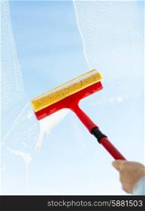 people, housework and housekeeping concept -close up of hand cleaning window glass with sponge mop and foam