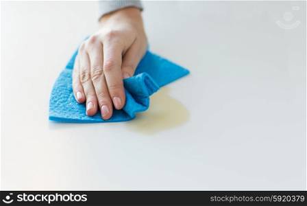 people, housework and housekeeping concept - close up of woman hand cleaning spot from table surface with cloth at home