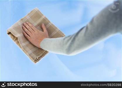 people, housework and housekeeping concept - close up of woman hand cleaning window glass with cloth