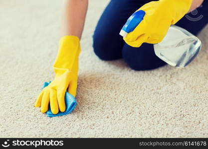 people, housework and housekeeping concept - close up of woman in rubber gloves with cloth and detergent spray cleaning carpet at home