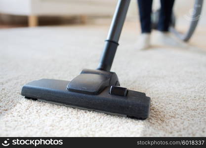 people, housework and housekeeping concept - close up of woman with legs vacuum cleaner cleaning carpet at home