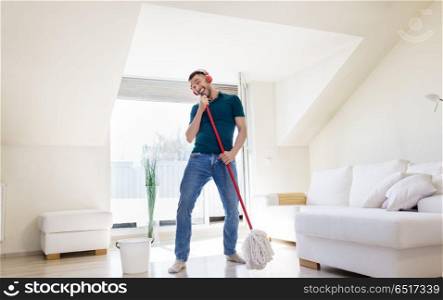 people, housework and housekeeping concept - happy man in headphones with mop cleaning floor and singing at home. man in headphones singing to by mop at home. man in headphones singing to by mop at home