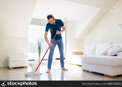 people, housework and housekeeping concept - happy man in headphones with mop cleaning floor at home. man in headphones cleaning floor by mop at home. man in headphones cleaning floor by mop at home