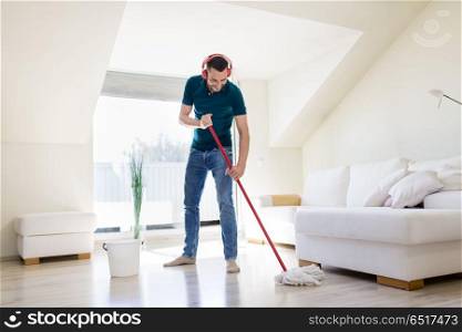 people, housework and housekeeping concept - happy man in headphones with mop cleaning floor at home. man in headphones cleaning floor by mop at home. man in headphones cleaning floor by mop at home